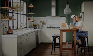 Two women sitting in a beautifully designed modern transitional kitchen looking at the best cabinet options on a computer.